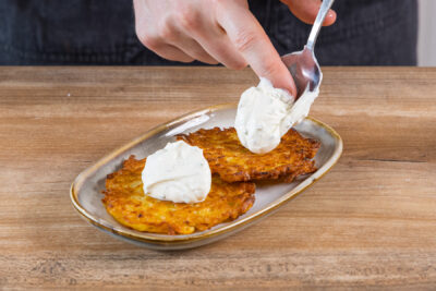 Crème fraîche auf den Kartoffelpuffern verteilen