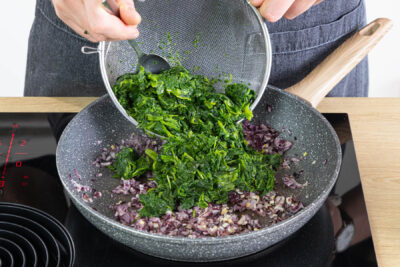 Spinat zu Zwiebel und Knoblauch geben