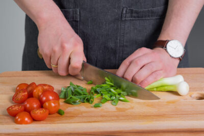 Die Tomaten und die Frühlingszwiebeln schneiden.
