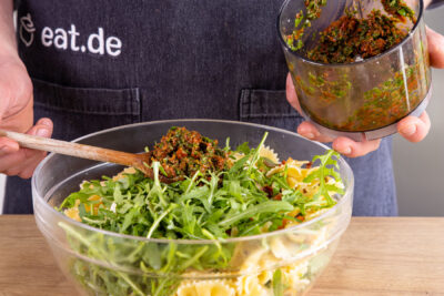 selbstgemachtes Pesto zum mediterranen Salat mit getrockneten Tomaten und Rucola geben