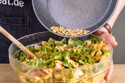 geröstete Pinienkerne zum mediterranen Salat mit getrockneten Tomaten und Rucola geben