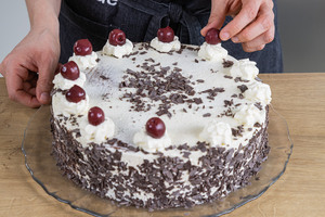 Die Schwarzwälder Kirschtorte nach Omas Rezept mit Sahne und Kirschen dekorieren