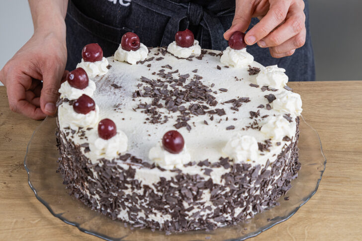 Die Schwarzwälder Kirschtorte nach Omas Rezept mit Sahne und Kirschen dekorieren