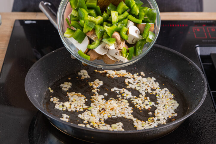 Paprika und Champignons in die Pfanne zu den Zwiebeln geben