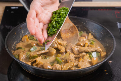 Petersilie zum Schweinegeschnetzeltes mit Champignons geben