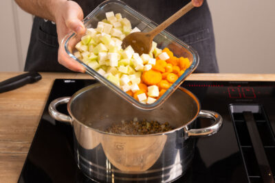 Gemüse in den Topf für den vegetarischen Linseneintopf geben