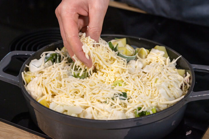 Blumenkohlauflauf mit Kartoffeln und Schinken mit Käse bestreuen