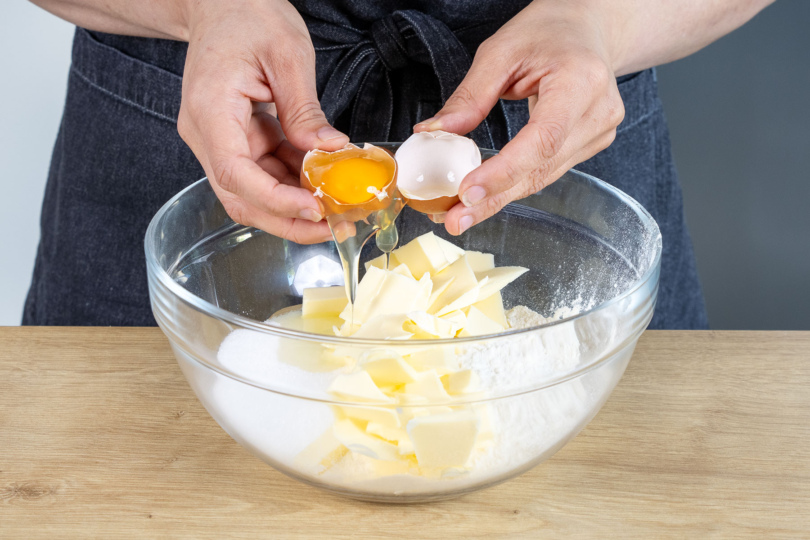 Ei zum Mehl, Zucker, Backpulver und Butter in die Schüssel geben