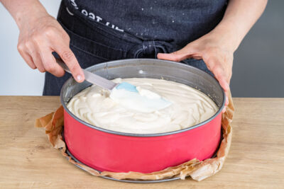 Käsekuchen-Masse auf Keksboden verteilen