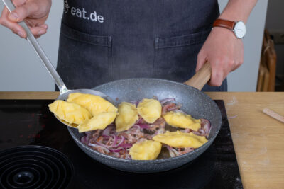 Die Kartoffel-Quark-Pierogi zu Zwiebeln und Bacon geben.