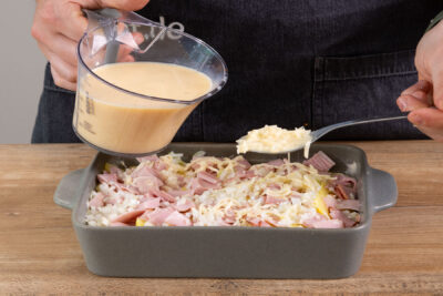 Die Masse mit Milch, Eiern und Käse über das Kartoffelgratin mit Schinken geben.