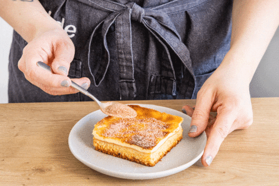 Zucker und Zimt über Schmandkuchen streuen