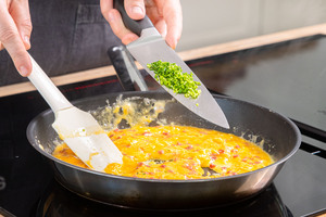 Schnittlauch zum Rührei mit Speck geben