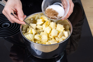 Zucker, Zimt und Nelke zu den Apfelstücken im Apfelsaft geben