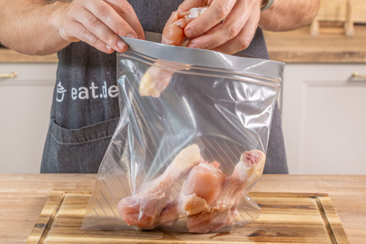 Hähnchenkeulen in einen Beutel geben