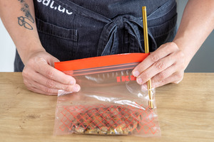 Luft mit Strohhalm aus einem Gefrierbeutel mit mariniertem Fleisch saugen