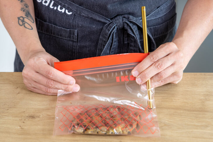Luft mit Strohhalm aus einem Gefrierbeutel mit mariniertem Fleisch saugen