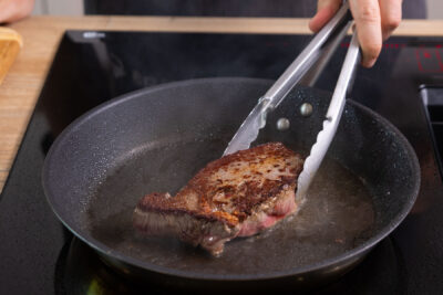 Rinderhüftsteak beim Braten wenden.
