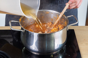 Gemüsebrühe zu dem Schweinegulasch gießen