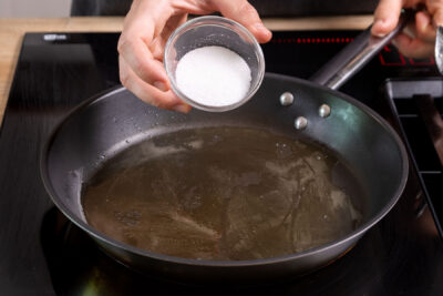 Zucker zum Butterschmalz in die Pfanne geben