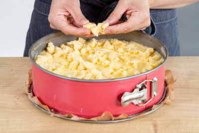 Streusel über dem Apfelkuchen mit Pudding verteilen