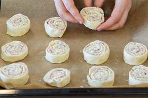 Herzhafte Blätterteigschnecken mit Käse und Schinken auf ein Backblech legen