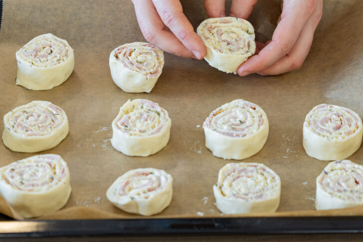 Herzhafte Blätterteigschnecken mit Käse und Schinken auf ein Backblech legen
