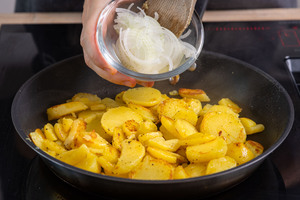 Zwiebeln zu den Bratkartoffeln geben
