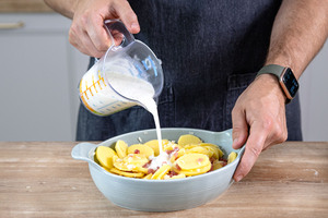 Soße ins Kartoffelgratin mit Speck geben