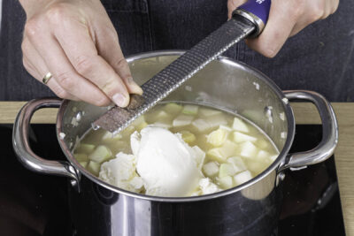Frischkäse und Gewürze zur Suppe geben