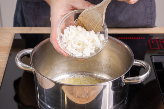 Zwiebelwürfel in den Topf geben