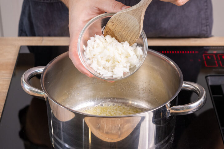 Zwiebelwürfel in den Topf geben