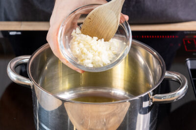 Zwiebel- und Knoblauchwürfel in den Topf geben