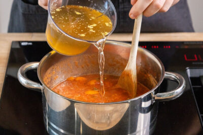 Gemüsebrühe zur Tomatensuppe gießen