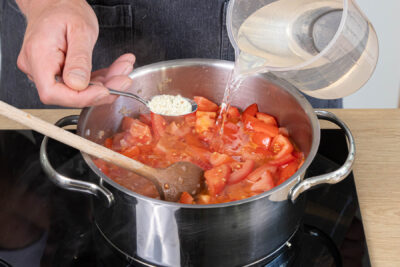 Wasser und Gemüsebrühpulver zu den Tomaten geben
