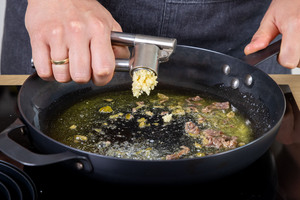 Knoblauch zu den Sardellen und Kapern in die Pfanne pressen