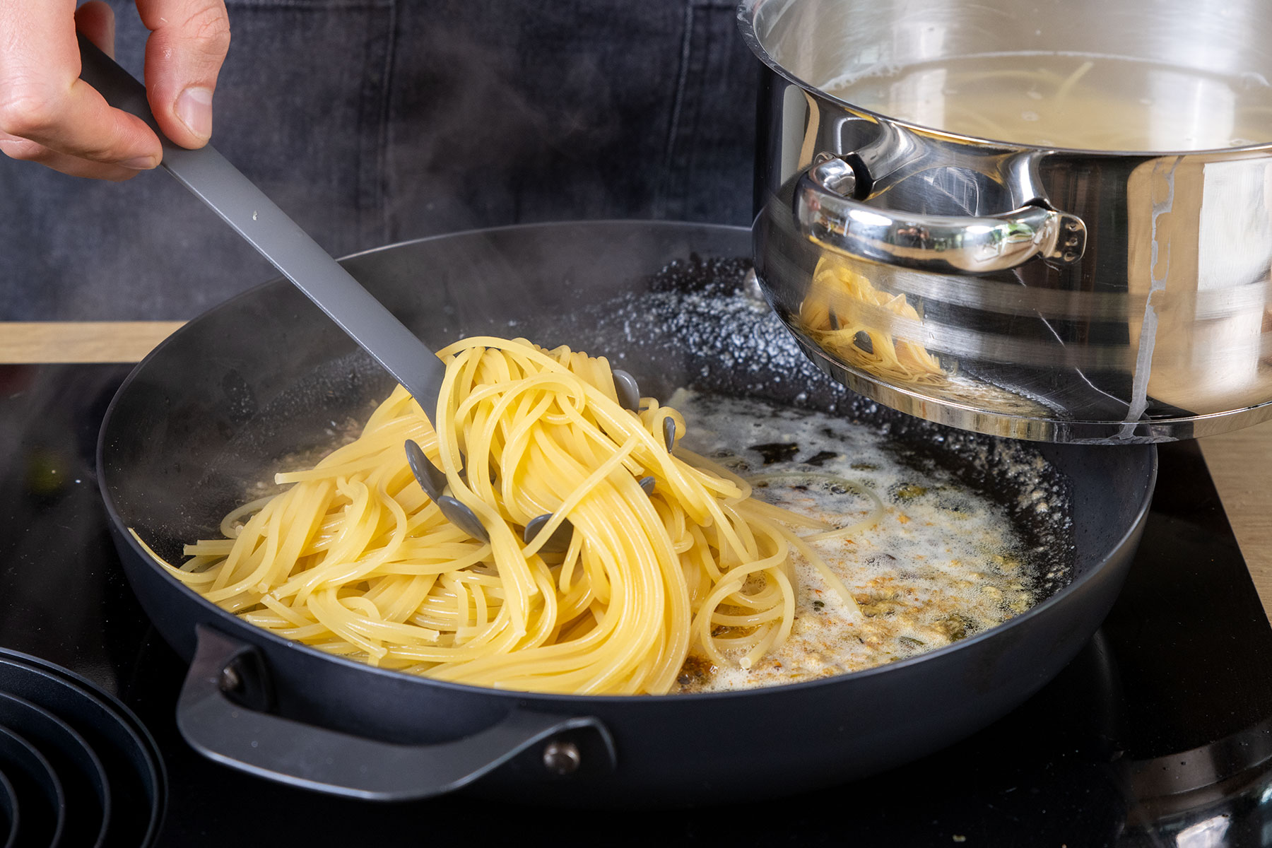 Spaghetti aus dem Topf in die Pfanne geben