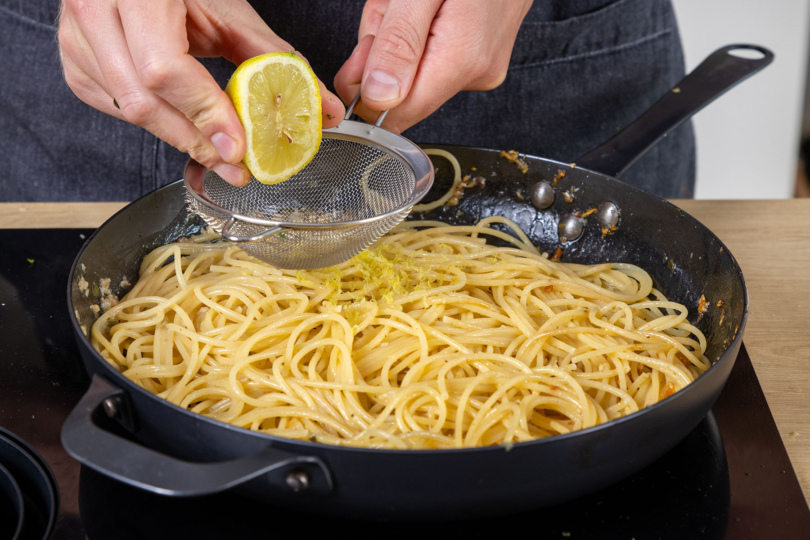Zitrone zu der Pasta mit Sardellen pressen