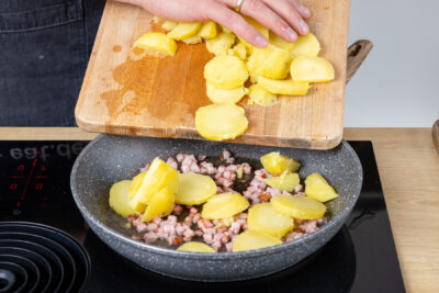 Kartoffelscheiben zum Speck in die Pfanne geben