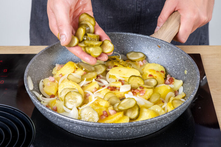 Die Gewürzgurkenscheiben  zum Berliner Hoppel Poppel in die Pfanne geben