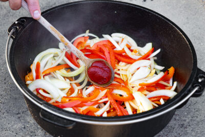 Tomatenmark zu Zwiebeln und Paprika geben.