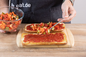 Tomaten und Paprika auf dem Baguette verteilen.