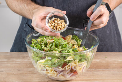 Pinienkerne zum italienischen Nudelsalat mit Rucola geben