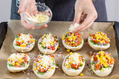 Käse auf den vegetarischen Pizzabrötchen verteilen