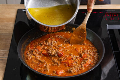 gehackte Tomaten und Gemüsebrühe zum Hackfleisch geben