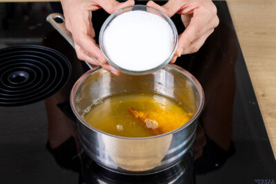 Zucker zu dem Orangensaft und Wasser in den Topf geben