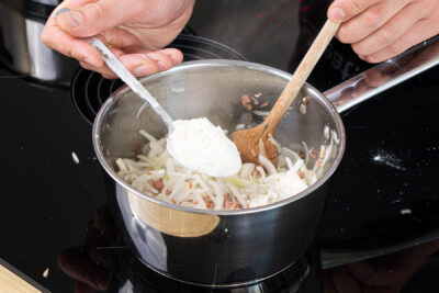 Mehl zu den angeschwitzten Zwiebeln geben