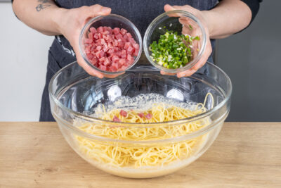 Schinken und Frühlingszwiebel zu den Spaghetti geben