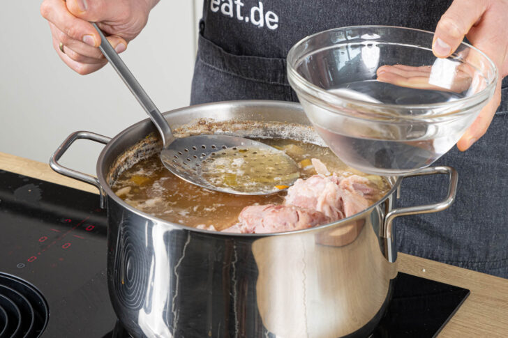 geronnenes Eiweiß vom Sud schöpfen