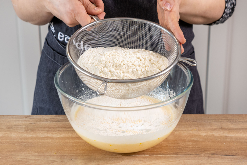Mehl und Backpulver zu der Zucker-Ei-masse sieben